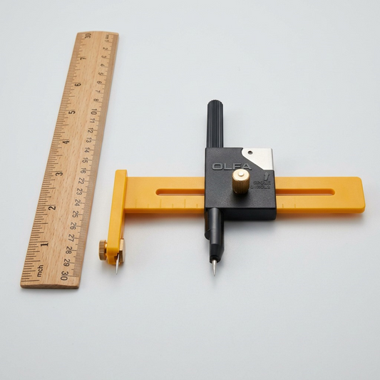 A close-up view of an Olfa CMP-1 compass cutter next to a wooden 30cm ruler, on a work surface.