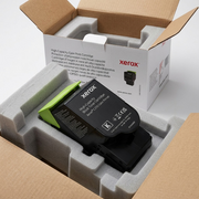 Premium, realistic photo: Xerox C310 black toner cartridge securely nestled in protective foam inserts inside a opened branded product box, showing protective transit.