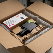 A premium, close-up photograph of the Xerox Magenta Standard Capacity Toner Cartridge, as seen in image_0.png, resting inside its open, padded cardboard retail shipping box. Custom-molded, recycled pulp inserts and protective air pillows are visibly securing the cartridge, demonstrating a secure and stress-free unboxing experience, all on a clean, light surface.