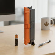 A compatible toner cartridge stands on a desk beside an AA battery and pen for a size comparison.