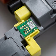 Macro close-up of the specific electronic chip and gold contacts on the Balloon Brand Compatible TN229XLY Yellow Toner. The precise green and yellow assembly is sharply focused, demonstrating compatibility engineering. No text is visible.