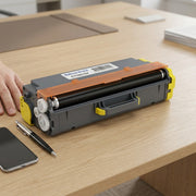 A photorealistic scale reference: a laser printer toner cartridge beside a smartphone and pen.