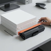 A photographic scale reference of the TN339BK toner cartridge on a cluttered office desk.
