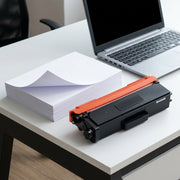 A reliable scale reference showing the toner cartridge next to standard A4 printer paper for context.