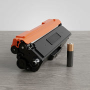 A TN436Y yellow toner cartridge placed prominently next to a standard AA-size battery for size reference.