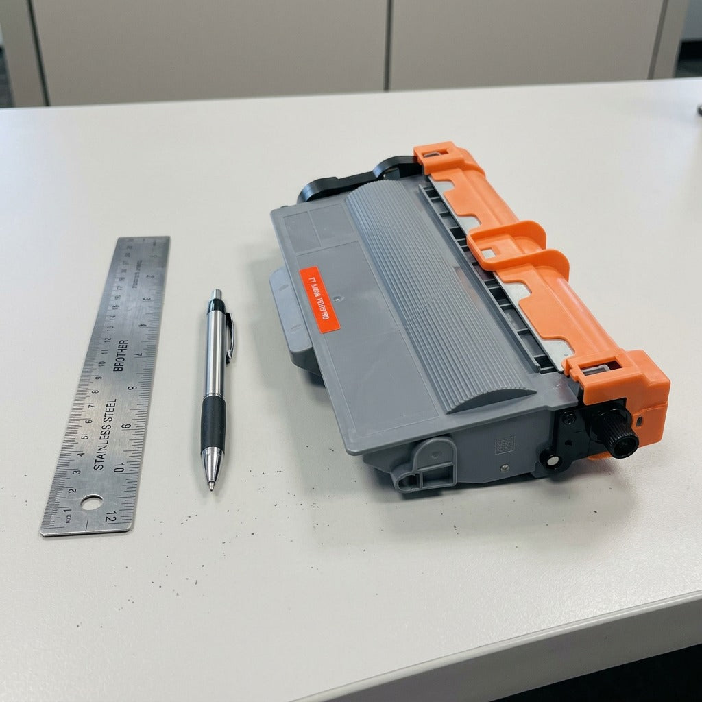 CTTN780 / CTTN750 toner cartridge next to standard metal ruler and ballpoint pen for size reference on desk.