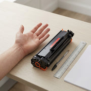 A close-up shot of a male hand next to a W1340X toner cartridge on a wooden desk.
