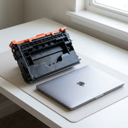 Product size reference showing the large W1470X toner cartridge on a desk next to a standard laptop.