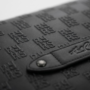 Extreme close-up of The Rolling Stones Paint It Black leather messenger bag's high-relief embossed 'RS' logo motif and signature brand plaque.