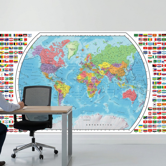 A professional workspace with the large Replogle world map displayer mounted on a white wall. The map's details, including country flags and French labels, are sharp. In the foreground, a modern desk holds supplies, with an ergonomic chair and a person's hand with a pen, providing a clear scale reference. Bright, natural light illuminates the clean environment, emphasizing the product's large size.