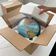 A Replogle Globemaster globe securely suspended by molded polystyrene foam within an open, thick cardboard shipping carton, showing premium protection.
