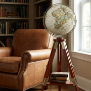 A photo of the Eaton III floor globe in a home library next to a leather armchair.