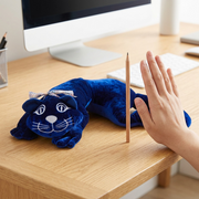 fdmt manimo Weighted Cat plush on a wooden desk next to a human hand and a standing pencil for scale reference.