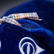 Macro view of the blue velvet texture, plaid bow, and eye embroidery on the weighted cat.