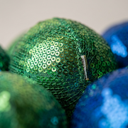 Extreme macro photo showing the tactile, sequined sensory fabric (sequins, a seam, and small tag) of an fdmt Stress Ball (MPN: 4050100).