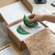 A hand with red nails lifts the green glitter fdmt manimo Half Moon Ball from its custom foam packaging.