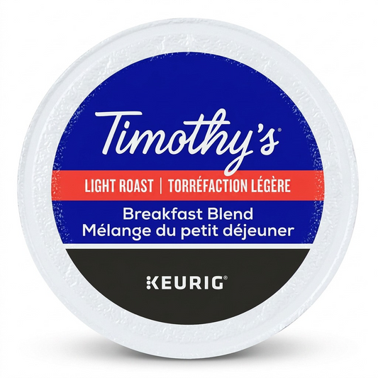 A professional, high-resolution product photograph showing the Timothy's Breakfast Blend K-Cup as seen in image_0.png, resting horizontally. The entire circular top label is visible, replicating the exact 'Timothy's' and 'Keurig' branding, color bands, and dual-language product descriptions for content and roast. It has a clean, natural shadow on a pure white background, showcasing all features sharply.