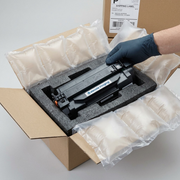 An Elevate Imaging toner cartridge sits securely inside a shipping box, protected by air pillows and foam inserts, ready for installation.