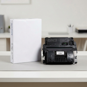 A large black laser toner cartridge is placed next to a standard ream of A4 printer paper for clear scale reference.