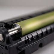 A macro photograph with a shallow depth of field, focusing on the texture and precise form of the toner cartridge's PCR development roller, showing the fine details of its green-yellow surface and metal shaft. An extreme close-up for product quality inspectio
