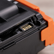 Macro extreme close-up of gold-plated chip contacts on black cartridge body, beside orange clip.