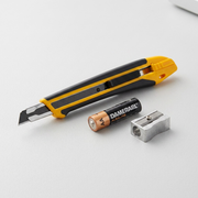 An extreme close-up photo comparing the Olfa XA-1 knife handle and blade to a standard AA battery.