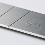 A macro photo of an OLFA 18mm snap blade, showing a snap line, the sharp, ground edge, and stamped text.