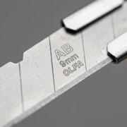 Extreme macro view of the original etched text on the silver steel snap-off utility blade.