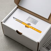 A close-up unboxing scene, with the OLFA 6mm AK-1/5B Art Knife resting on a white, recessed foam insert.