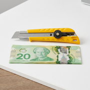 A visual comparison image of the L-1 utility knife beside a stack of Canadian currency.