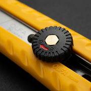 Macro shot of the ratchet lock dial on the Olfa L-1 utility knife, showing textured grip and mechanism.
