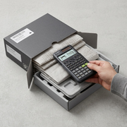 Hand unboxing a black Casio FX-300ESPLS2 scientific calculator from secure shipping packaging.