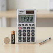 Casio HS-8VA handheld calculator shown on a desk beside an AA battery, coin, and pen for scale.