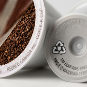 Macro photograph focusing on the detailed texture of raw coffee beans and the recyclable icon on the K-Cup pod.
