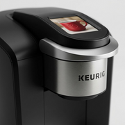 A macro photo of the Keurig K3550's brew head and display, highlighting brushed metal and touchscreen details.