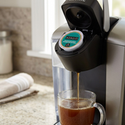 A Keurig K-Cup machine with a brewed Adagio House Blend Decaf coffee in a glass mug.