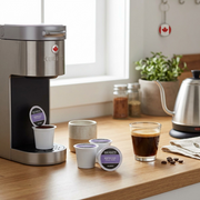 A photo of an espresso machine and cup next to Van Houtte K-Cup capsules on a wooden countertop.