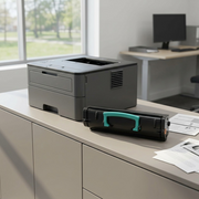 A detailed photograph of the black toner cartridge with its teal handle, resting next to a modern office printer.