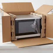 A realistic photo of the Sharp SMC1464KSC microwave being securely unboxed on a wooden countertop.