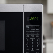 A macro close-up image showing a stainless steel microwave control panel with a digital clock and various buttons.