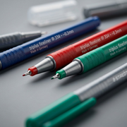 A macro view of two STAEDTLER triplus fineliner points, showing precise ~0.3mm metal-clad felt tips and textured triangular grips.