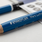 Extreme close-up macro view of the STAEDTLER Mars Lumograph pencil, showing the blue lacquered wood texture and crisp silver embossed lettering.
