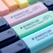 Extreme, shallow depth-of-field close-up on textured STAEDTLER Textsurfer pastel highlighters' ink bodies and logos.