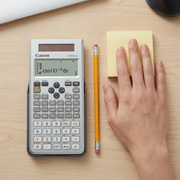Canon F-792SGA scientific calculator on a desk next to a pencil and a hand for size comparison.