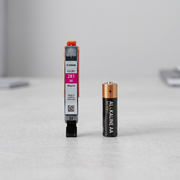 The Canon CLI-281 Magenta ink cartridge is positioned next to a standard AA battery for scale comparison.