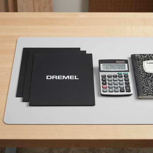 Three Dremel 3D40 build sheets stacked next to a calculator and notebook for size reference.