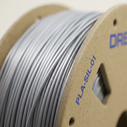 Macro close-up of precise, uniformly wound Dremel silver 1.75mm PLA filament on a cardboard spool.