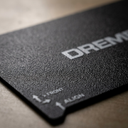 Extreme macro close-up of a Dremel 3D40-FLX flexible build sheet's textured printing surface with Dremel logo.
