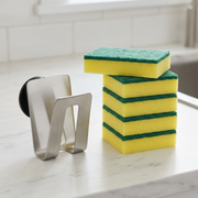 A scale visual of the Happy Sinks stainless steel sponge holder next to standard kitchen sponges.