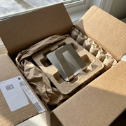 An open cardboard mailing box reveals the stainless steel sponge holder, securely cushioned in protective kraft paper and a corrugated insert, showcasing damage-free delivery.